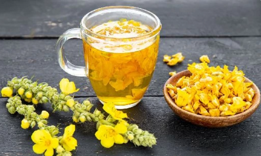 Tasse de thé à la molène entourée de fleurs de molène fraîches et séchées, avec un bol en bois contenant des fleurs séchées et des tiges de molène en arrière-plan.