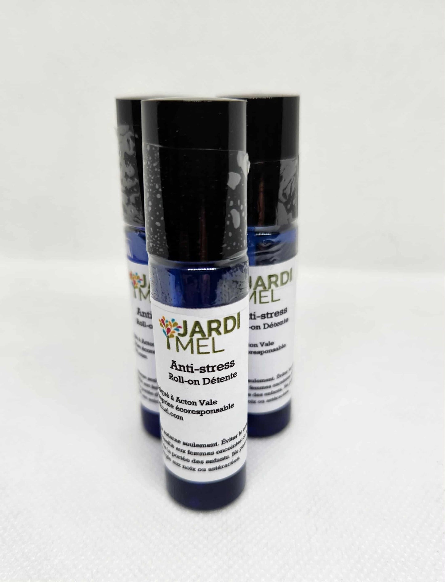 Trois flacons bleus de roll-on « Anti-stress » de la marque Jardi Mel, disposés côte à côte sur un fond blanc. Les étiquettes indiquent qu’il s’agit d’un produit naturel et écoresponsable fabriqué à Acton Vale.