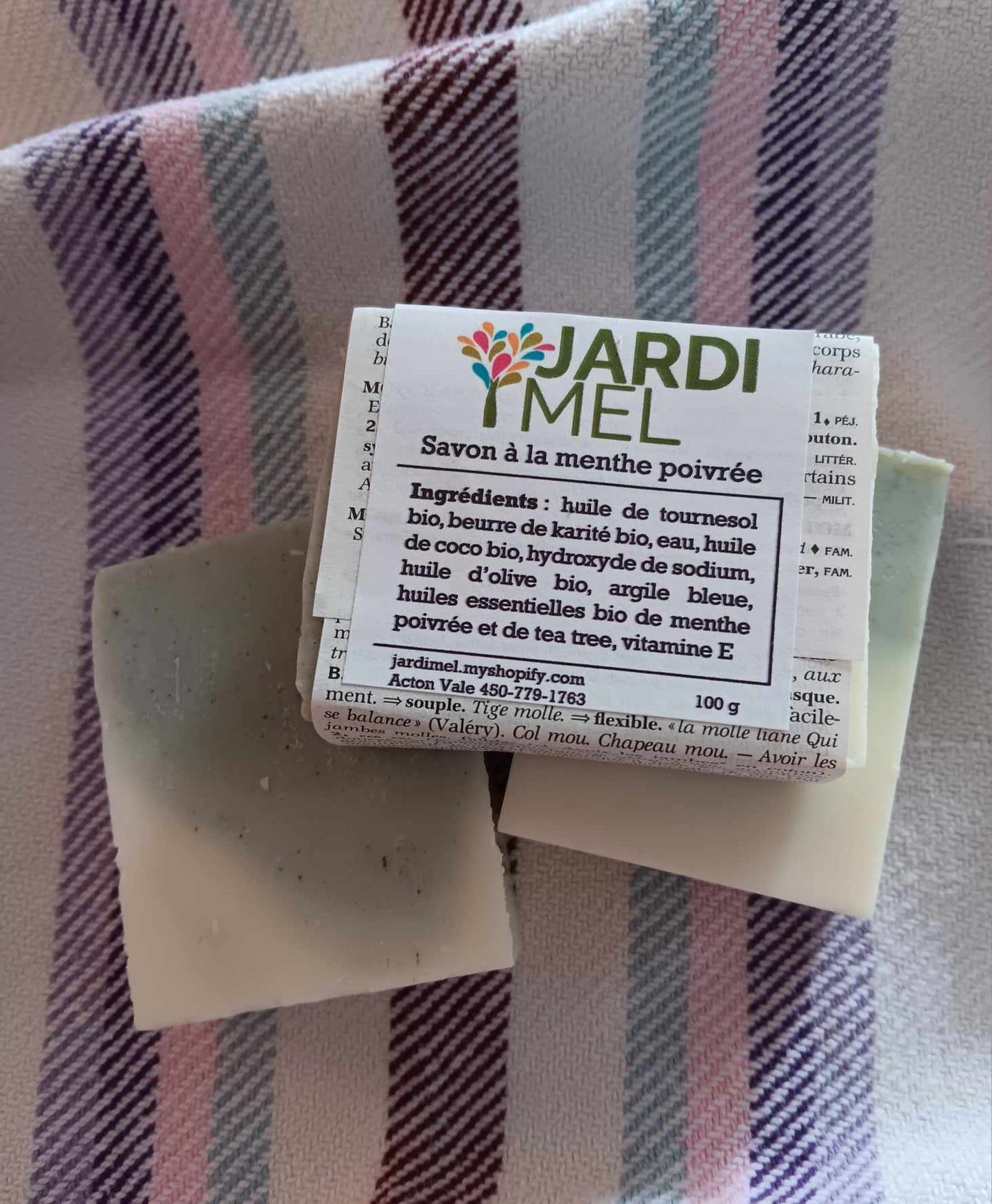 Savon artisanal Jardi Mel à la menthe poivrée, posé sur un tissu coloré. Contient des ingrédients bio : huile de tournesol, beurre de karité, huile de coco, huile d'olive, et huiles essentielles de menthe poivrée et de tea tree. Étiquette avec jardimel.com