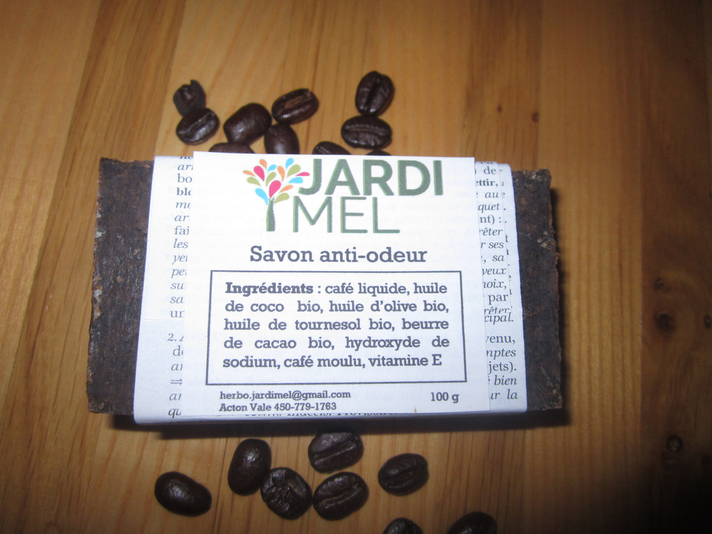 Savon artisanal JARDI MEL "Savon anti-odeur", fabriqué avec des ingrédients biologiques tels que café liquide, huile de coco, huile d'olive, huile de tournesol, et beurre de cacao. Le savon de 100 g est entouré de grains de café, posé sur une surface en bois. Étiquette avec l'inscription jardimel.com