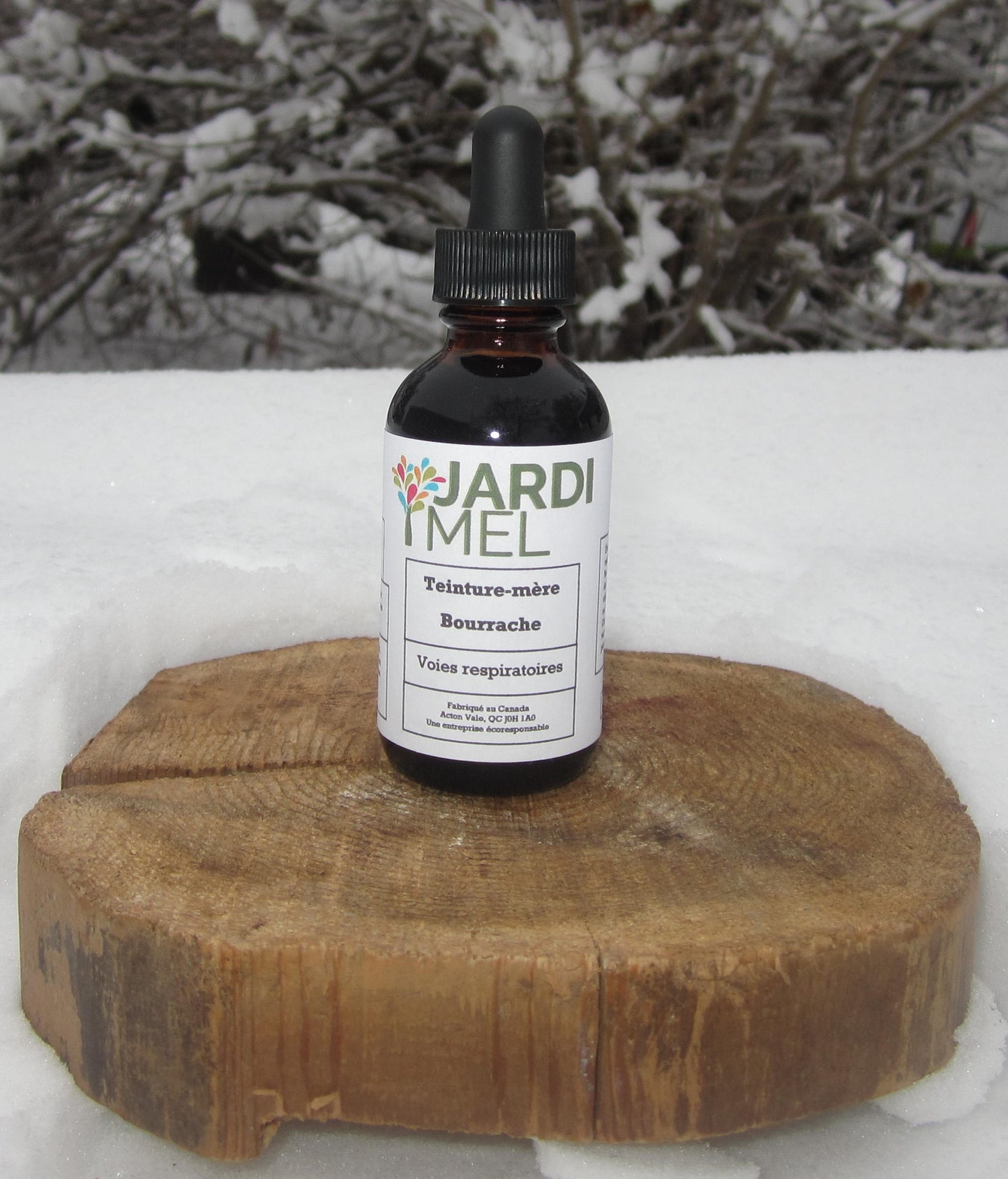 L'image montre une bouteille de teinture mère de la marque JARDI MEL posée sur une tranche de bois, avec un fond enneigé. L'étiquette de la bouteille indique qu'il s'agit d'une teinture mère de bourrache, utilisée pour les voies respiratoires. Le produit est fabriqué au Canada, jardimel.com