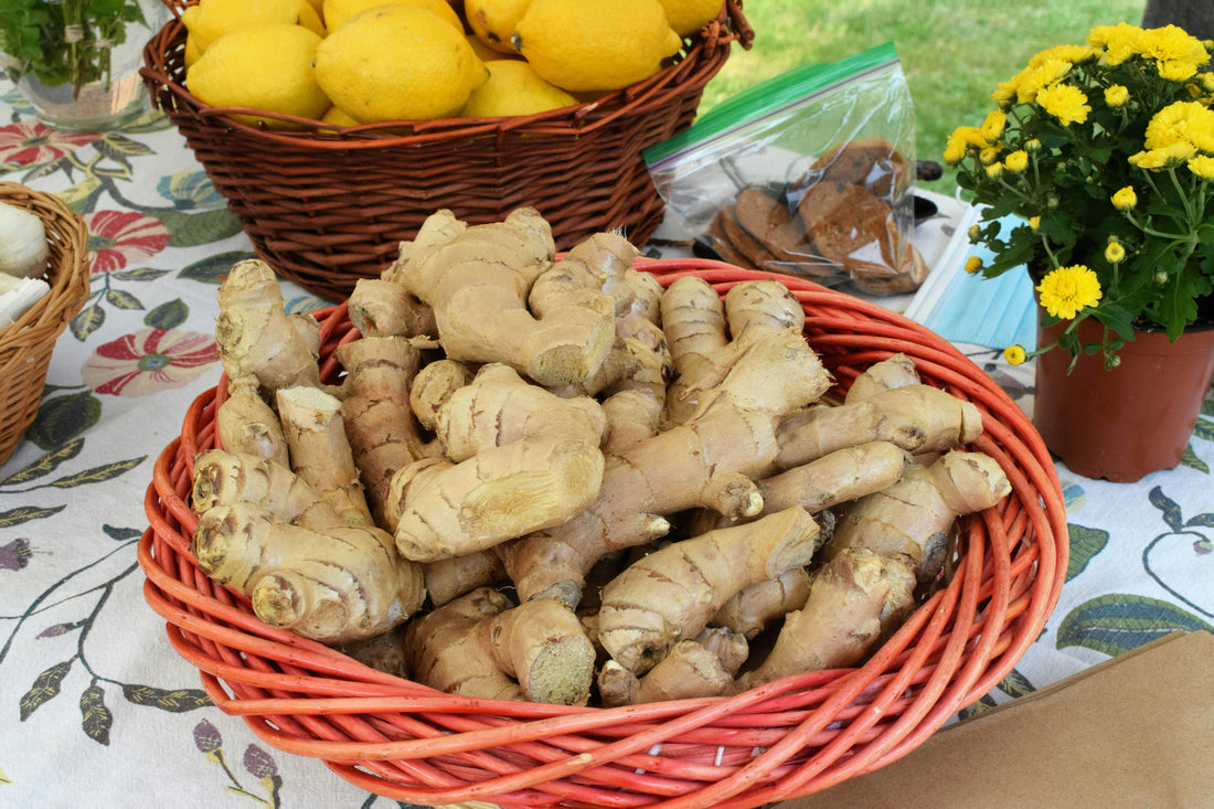 Un panier en osier débordant de racines de gingembre fraîches, avec des citrons jaunes et des champignons séchés à proximité, le tout décoré par un pot de fleurs jaunes. Une scène qui évoque la richesse de la nature.