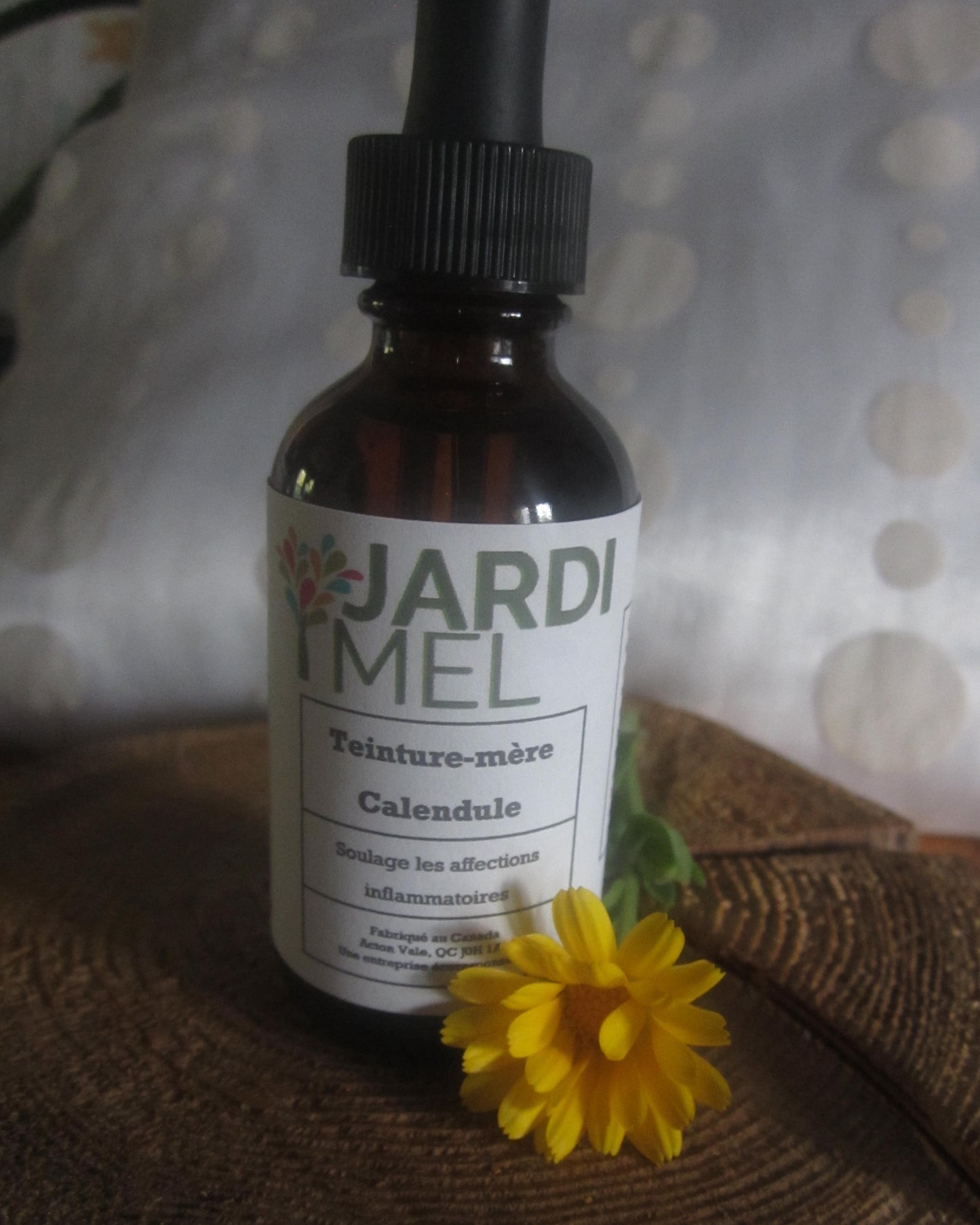 Une bouteille de teinture mère de Calendula, produit par JARDI MEL avec une fleur de calendule jaune à l'avant de la bouteille.